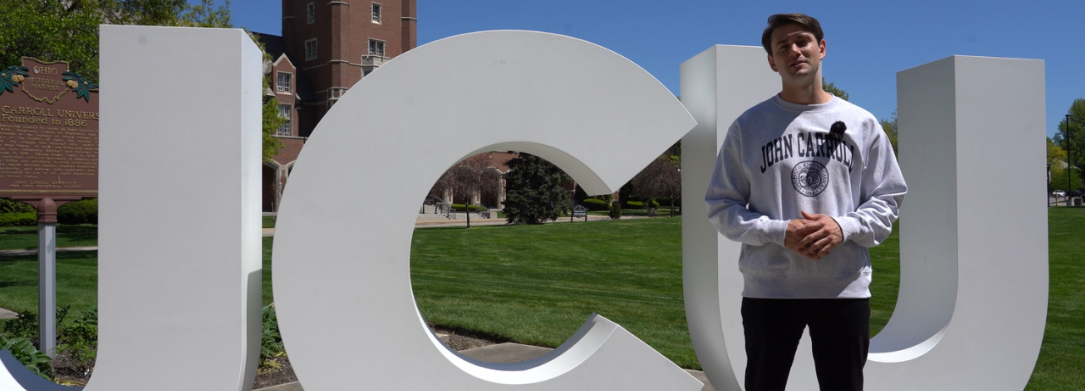 Graduate School Virtual Tour Guide Michael in front of JCU block letters on campus